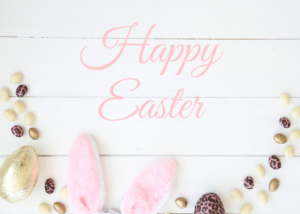 Easter greeting with chocolate eggs and bunny ears on a white wooden background