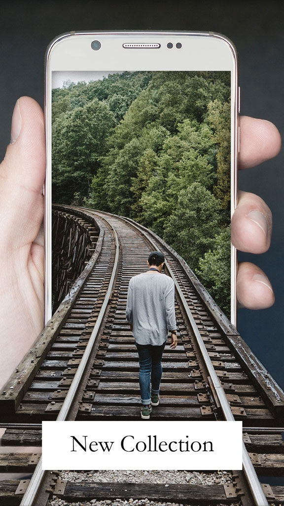 A hand holding a mobile phone displaying a man walking on train tracks surrounded by a lush forest.