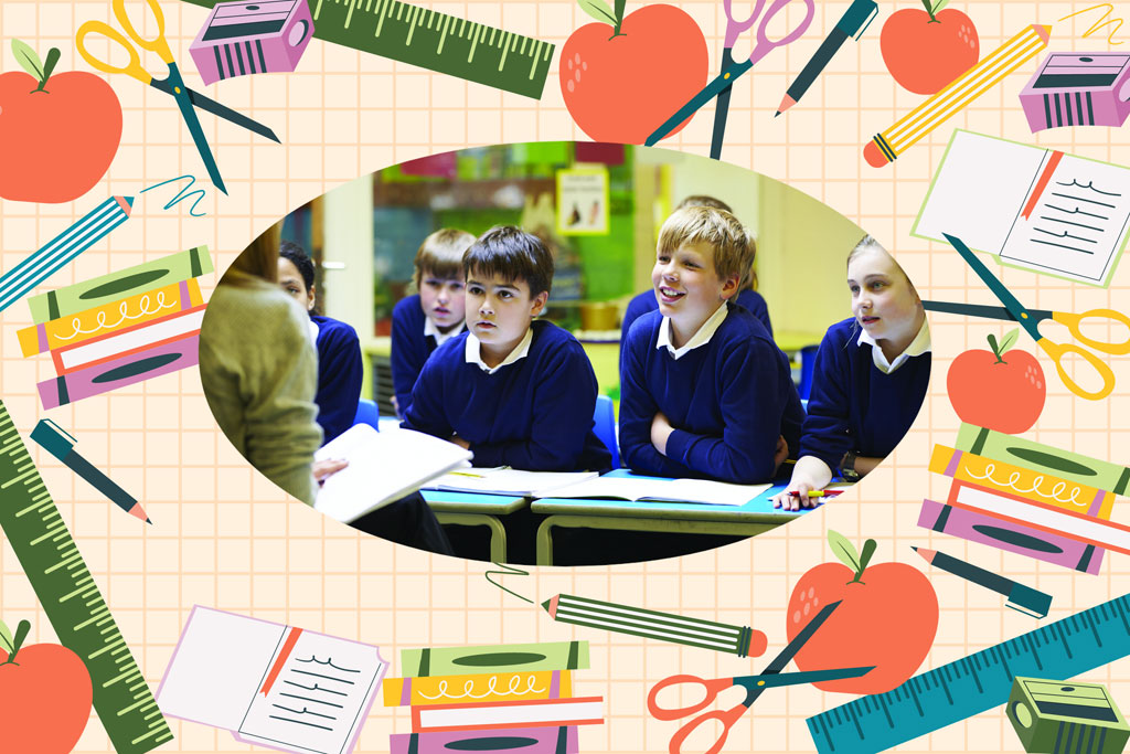 Children in blue uniforms sitting at a desk with a teacher nearby