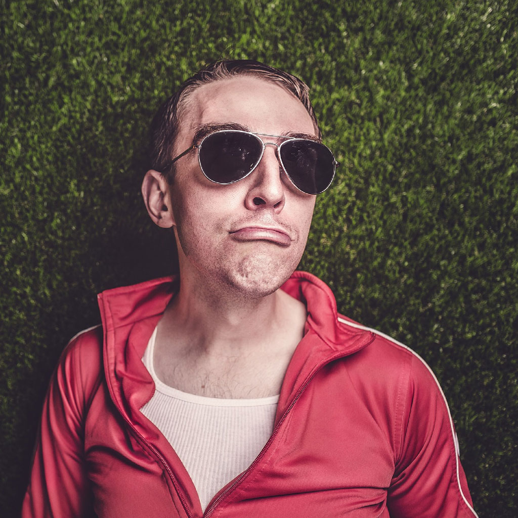 Man in red jacket and sunglasses against a green hedge