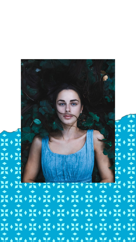 Woman lying down surrounded by leaves wearing a blue dress