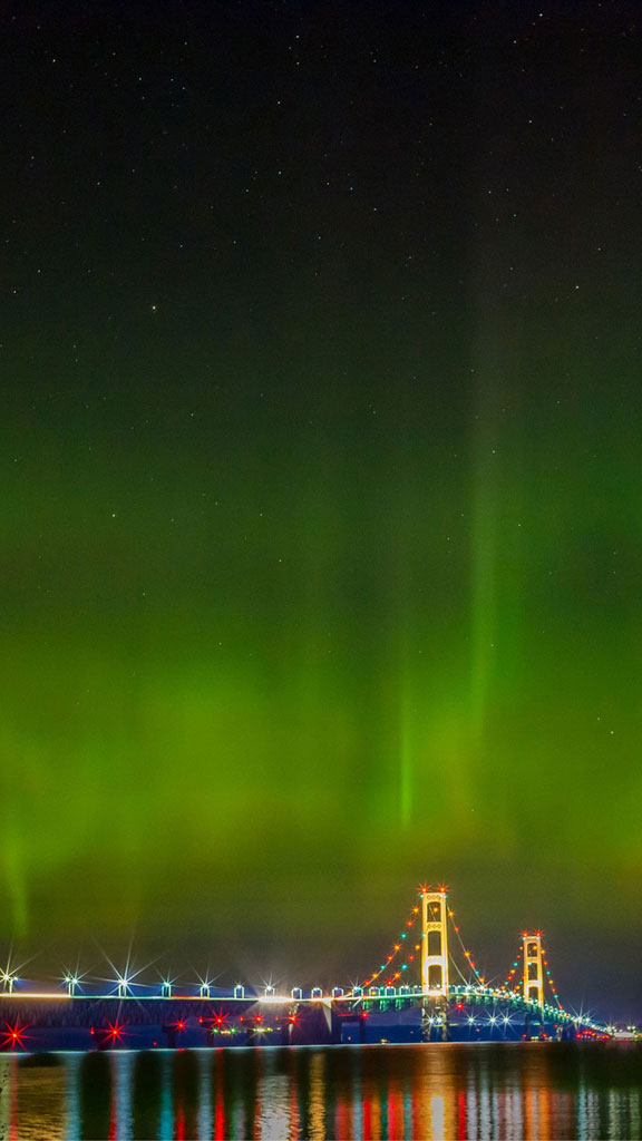 Mackinac Bridge lit up at night with the Northern Lights visible in the sky