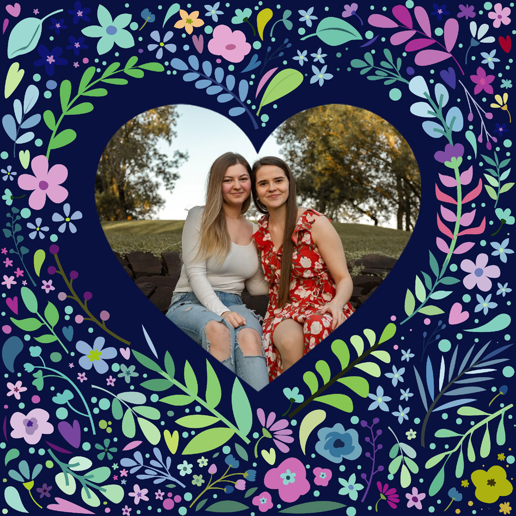 Two women sitting together in a heart-shaped frame surrounded by flowers