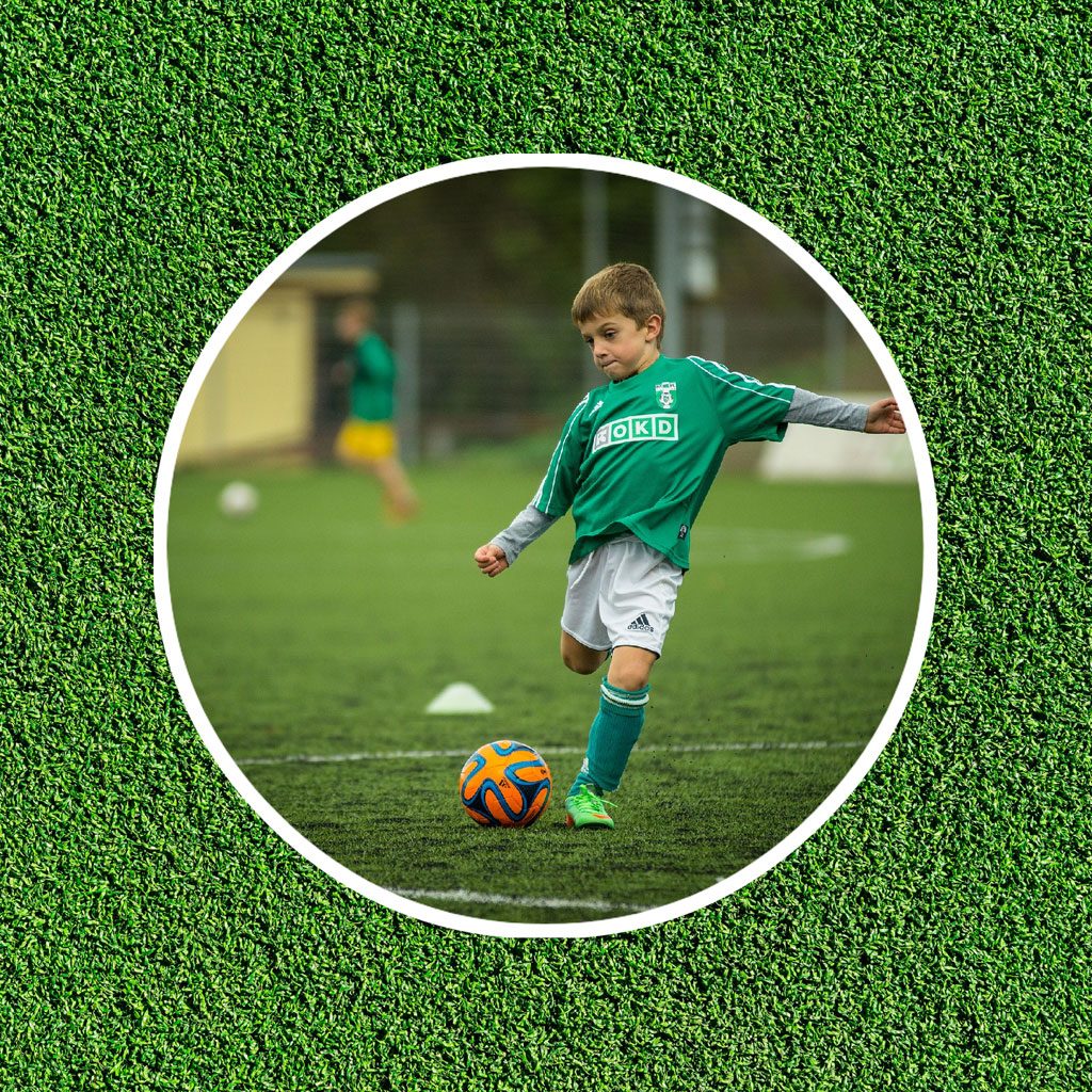 A young boy kicking a soccer ball on a green field