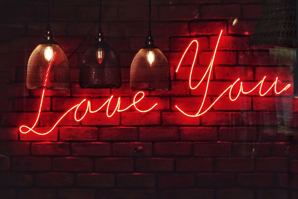 Red neon 'Love You' sign on a brick wall with pendant lights.