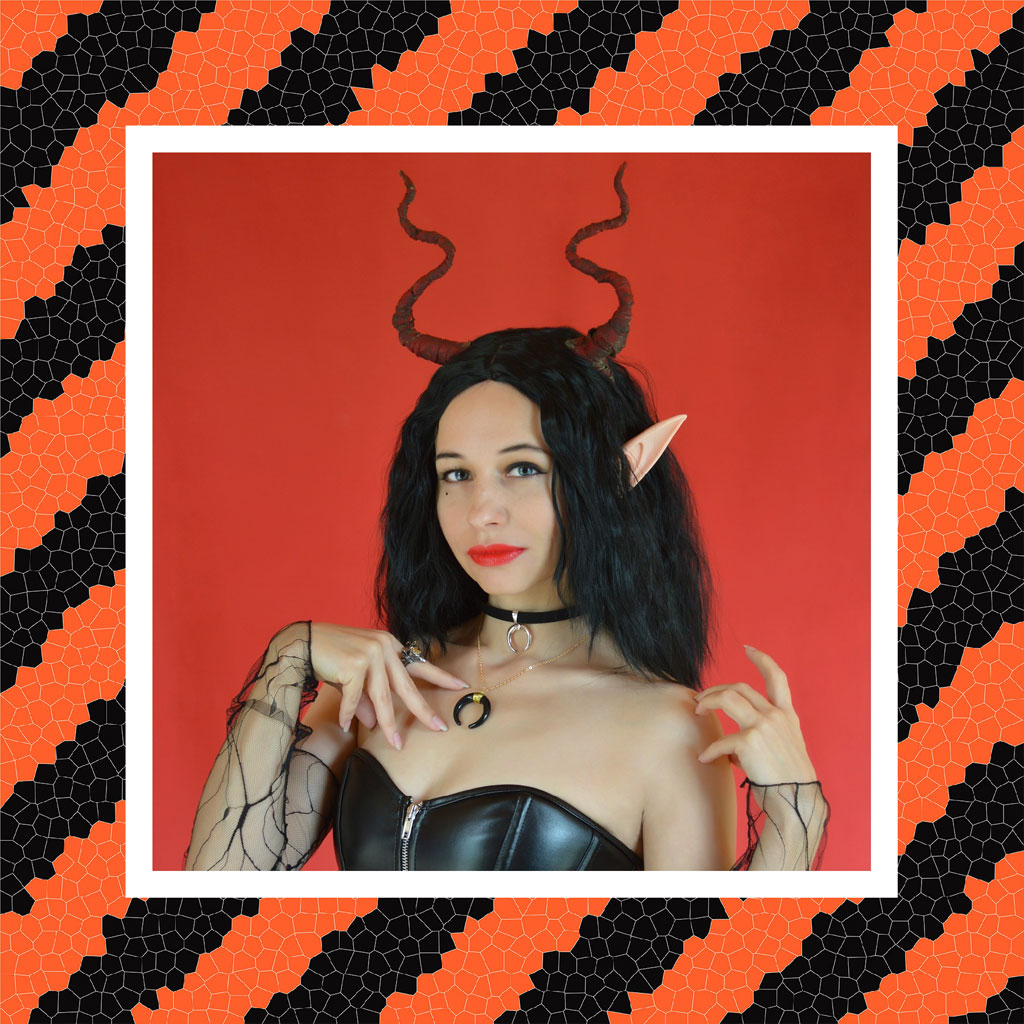Woman with devil horns and black leather top posing in front of a red backdrop