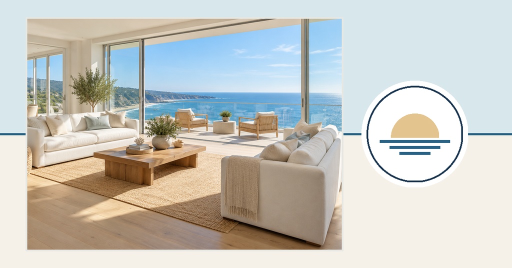 Bright living room with sofas facing a large window and ocean view beside a circular sunset logo
