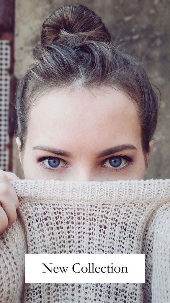 Woman with blue eyes and dark hair in a bun, wearing a beige sweater