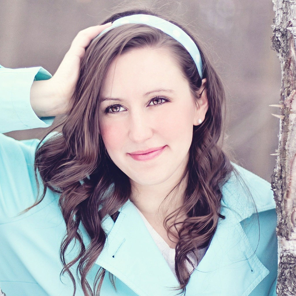 A young woman with long brown hair wearing a light blue jacket and a white headband.
