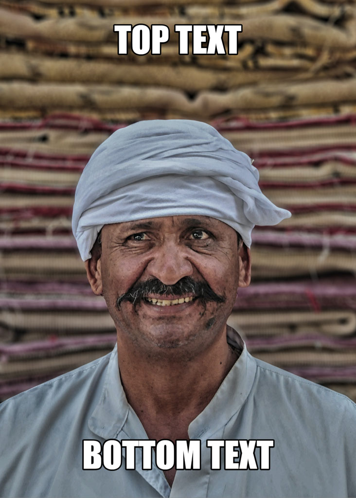 Man with a mustache and turban in front of a stack of rugs or mats