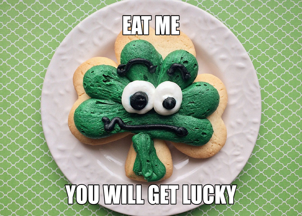 A shamrock-shaped cookie with a face, on a white plate against a green background