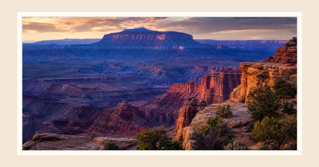 Wide desert canyon landscape with mesas and warm sunset light over rocky cliffs.