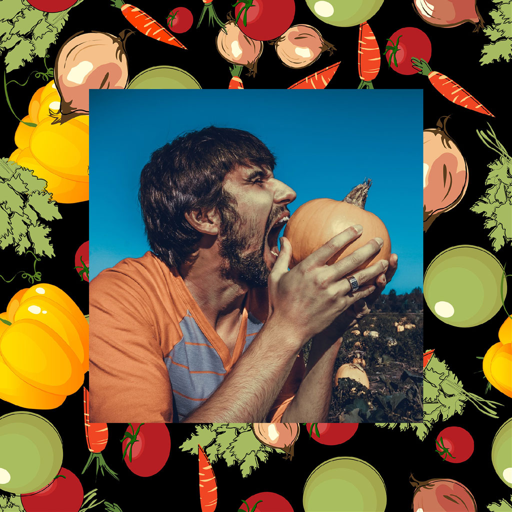 Man biting into a raw onion surrounded by colorful vegetables