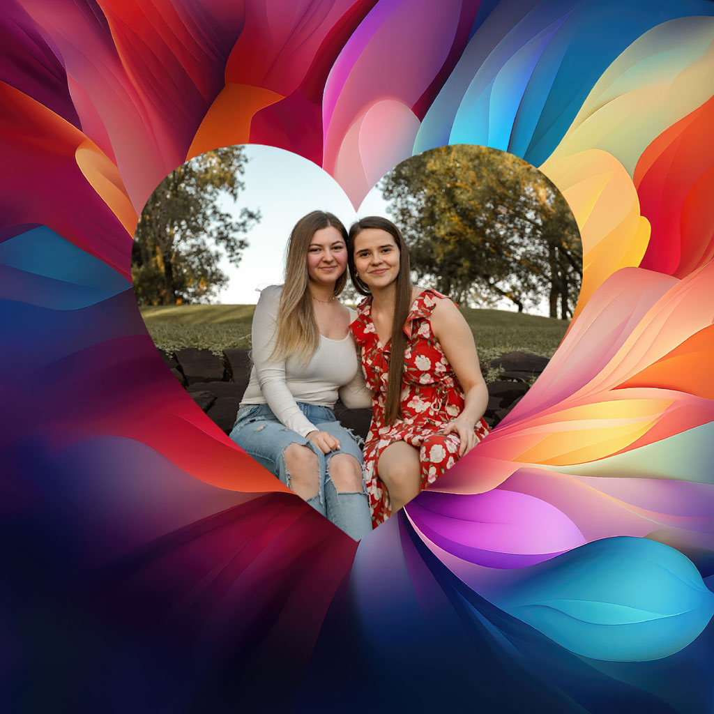 Two women sitting together in a heart-shaped frame surrounded by colorful petals
