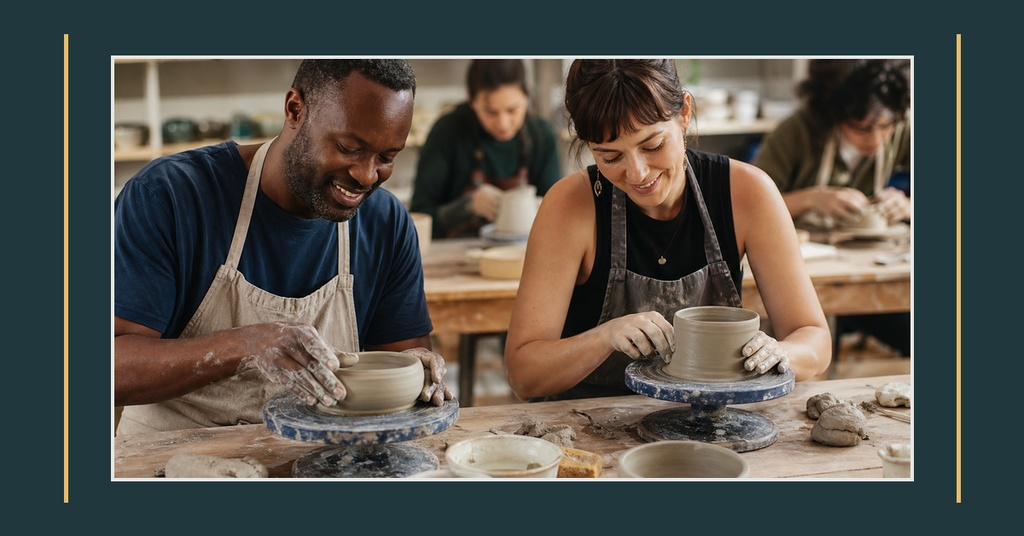 Three people shaping pottery at a workshop table in a dimly lit studio.