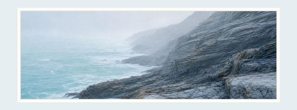 Wide coastal cliffs beside a calm ocean under a pale sky.