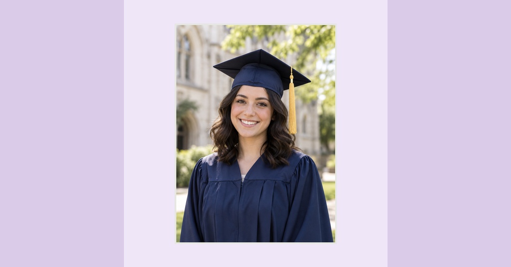 Smiling graduate in navy cap and gown standing outdoors on a campus walkway.