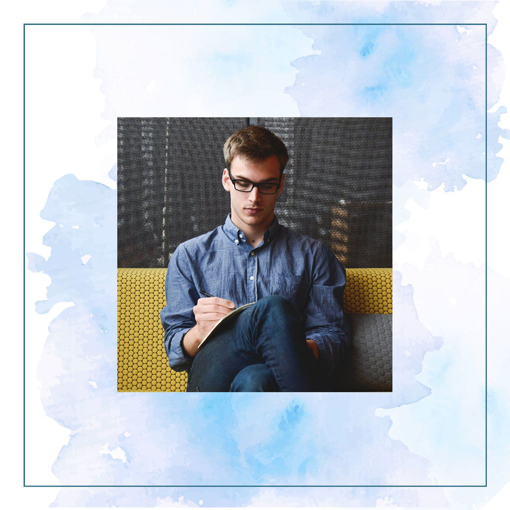 Man in blue shirt writing in notebook on yellow couch