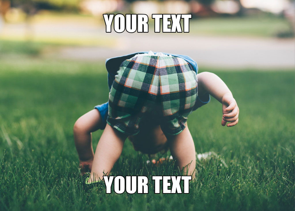 A toddler in a plaid hat and blue shorts is crawling on all fours in a grassy field.