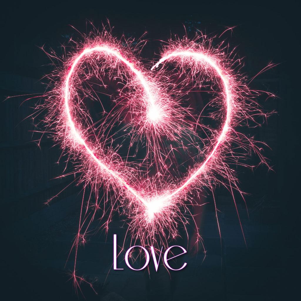 A heart shape created with sparklers against a dark background with the word love written in pink.